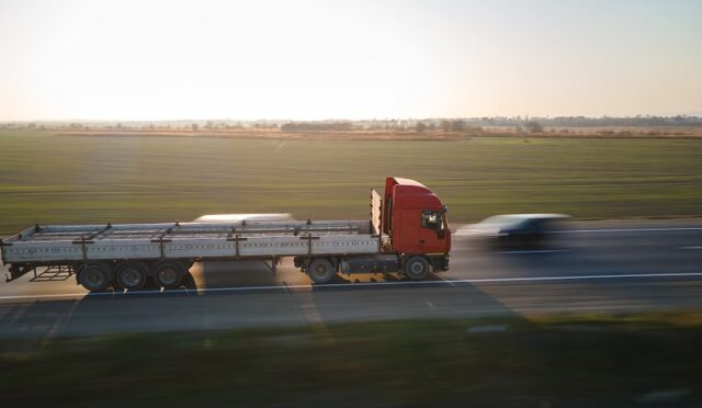 Aerial view of blurred fast moving semi-truck with cargo trailer driving on highway hauling goods in evening. Delivery transportation and logistics concept